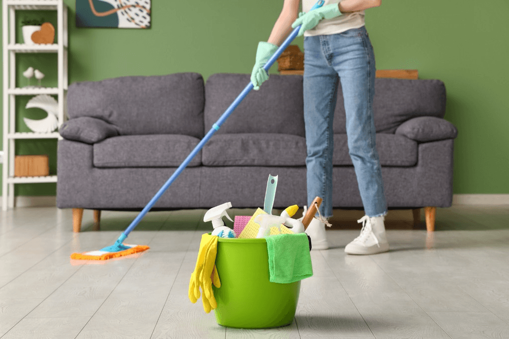 Cleaner mopping a wood floor with a bucket of cleaning supplies in the foreground